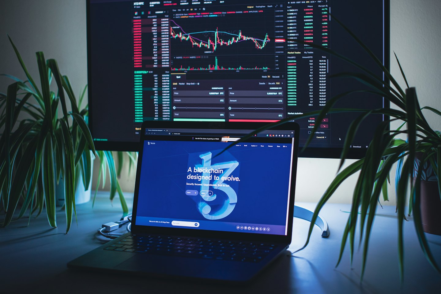 Laptop e monitor che mostrano grafici di criptovalute su una scrivania.