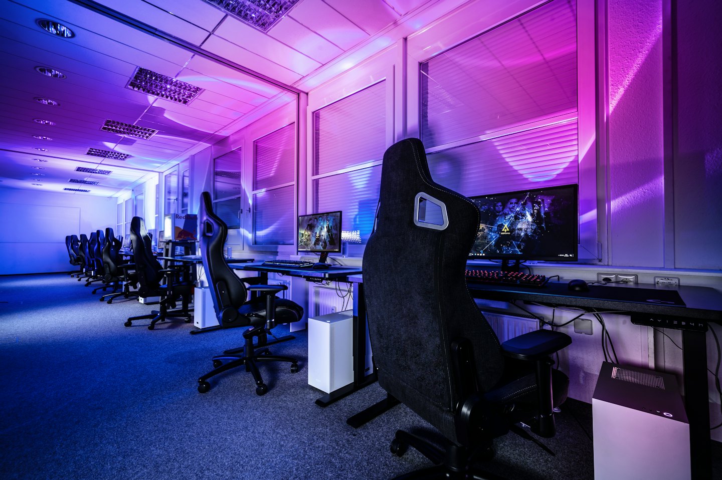 Fila di postazioni per computer da gaming vuote con sedie e monitor.